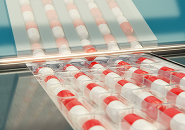 Close-up of an automated pharmaceutical packaging line where red and white capsules are sealed in transparent blister packs. The blister packs move along a conveyor under a clear protective cover, illustrating the precision and efficiency of primary packaging processes relevant to Extractables & Leachables testing by Eurofins BioPharma Product Testing.