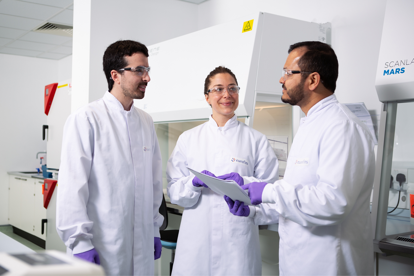 Scientists in a laboratory discussing the production and banking of microbial strains, with specialized equipment in the background.