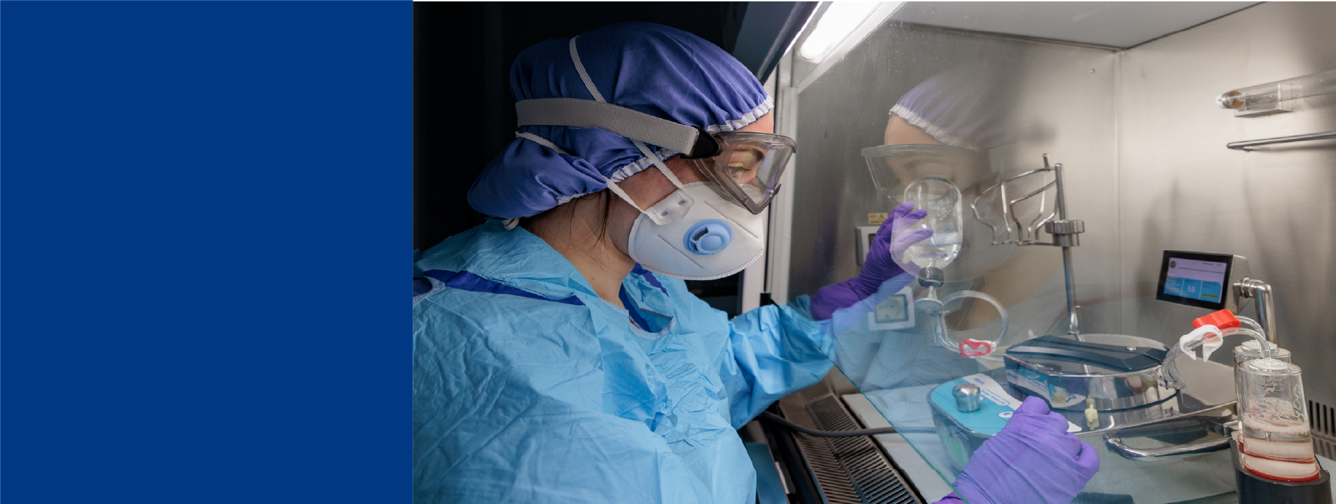 Scientist in protective gear using sterility testing equipment in a sterile product testing lab.