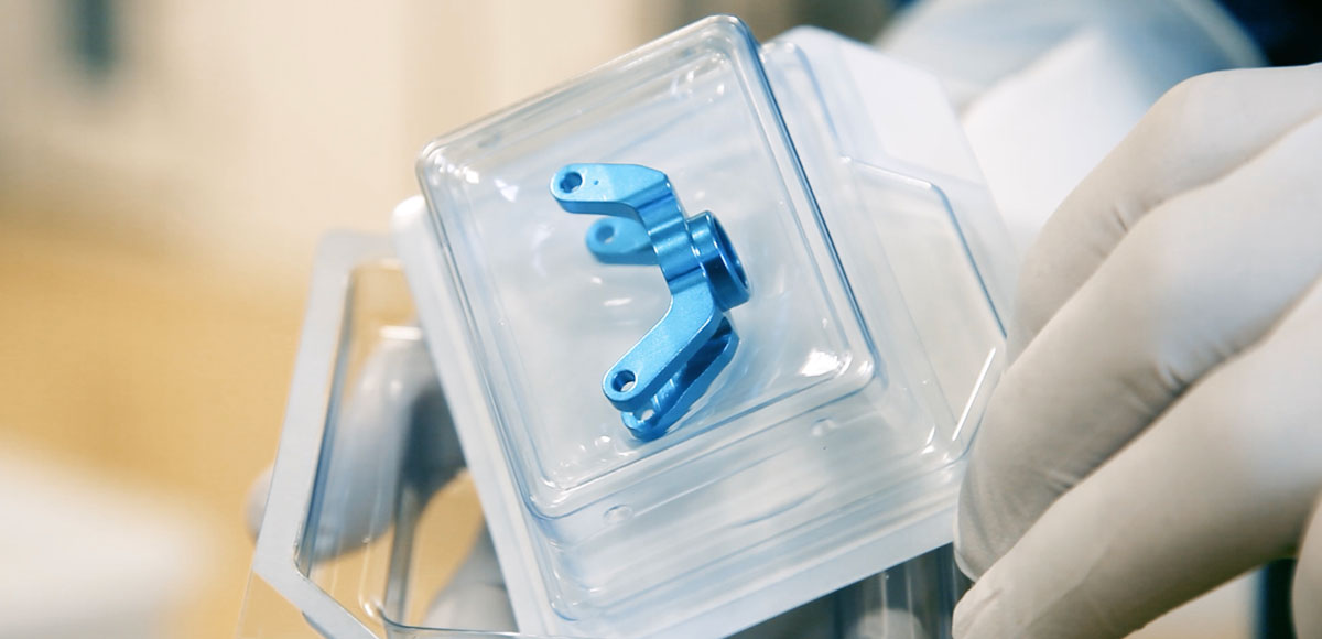 Blue metallic medical device with two arms, each featuring a hole at the end, placed inside a sealed blister.