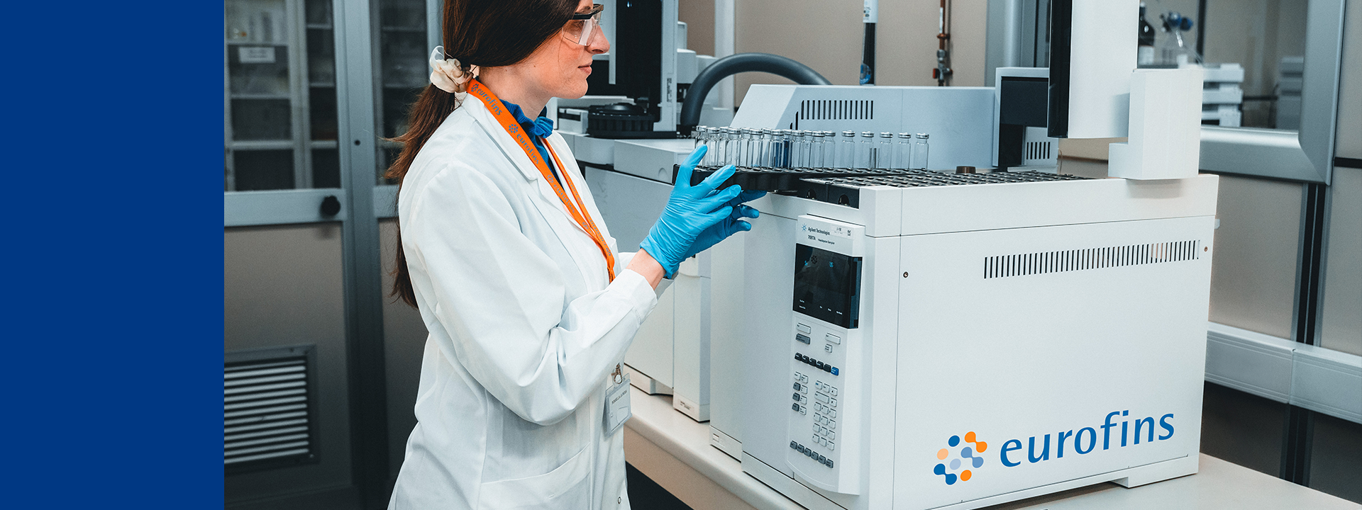 Eurofins BioPharma Product Testing laboratory setting with a technician wearing a white lab coat and blue gloves, operating a piece of equipment. The technician is handling test tubes or vials placed in the machine. This environment is focused on pharmaceutical gas testing, where gases used in pharmaceutical processes are analysed for purity, composition, and contaminants to ensure they meet stringent quality standards.