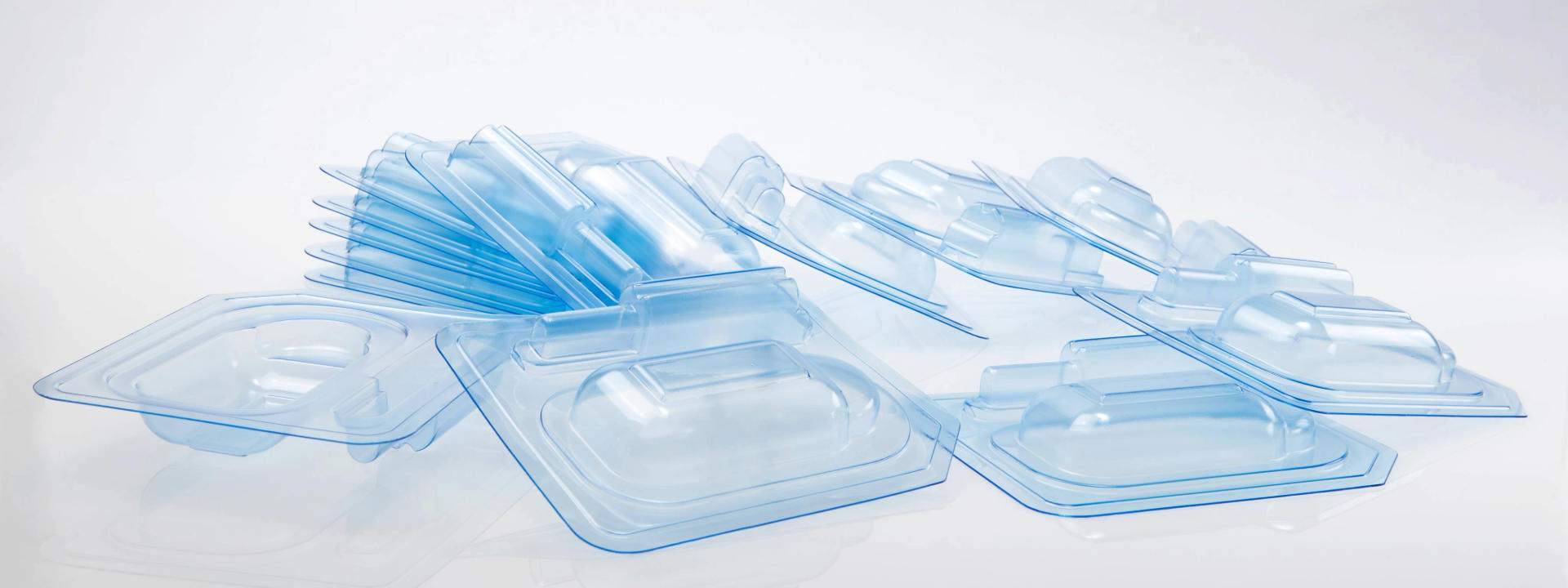 Collection of transparent blue-tinted blister packaging trays, stacked and overlapping, likely designed for holding small medical or electronic components.