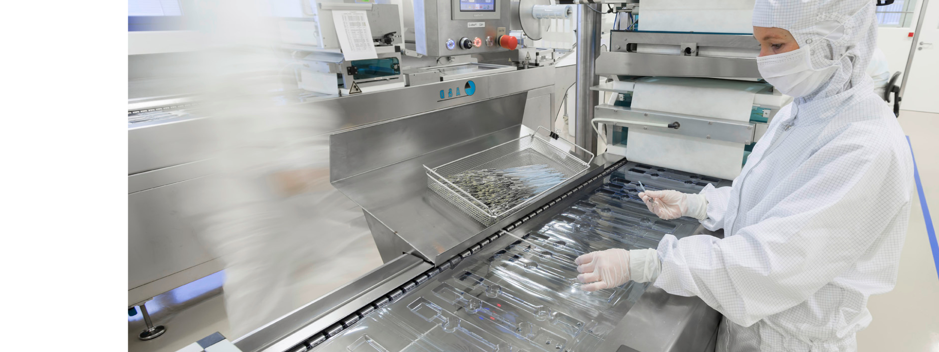 Production machine manufacturing sterile blister packaging with cleanroom personnel in the background