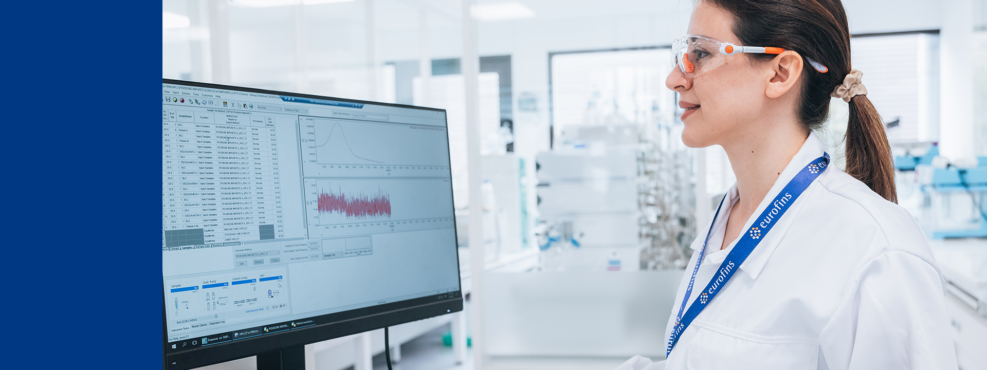 A laboratory scientist wearing a white lab coat and blue gloves is seated at a workstation at Eurofins BioPharma Product Testing laboratory, analyzing data on a computer screen. The display shows scientific graphs and tables, suggesting the evaluation of physical and chemical properties of pharmaceutical solids. The setting reflects a controlled laboratory environment dedicated to solid state characterization services, such as polymorph analysis, particle size distribution, and crystallinity assessment.