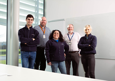 Five members of the MDS Consulting team standing in a bright office with large windows and a whiteboard, faces blurred for privacy, representing expert support in Quality Assurance, Regulatory Affairs, and PRRC services.