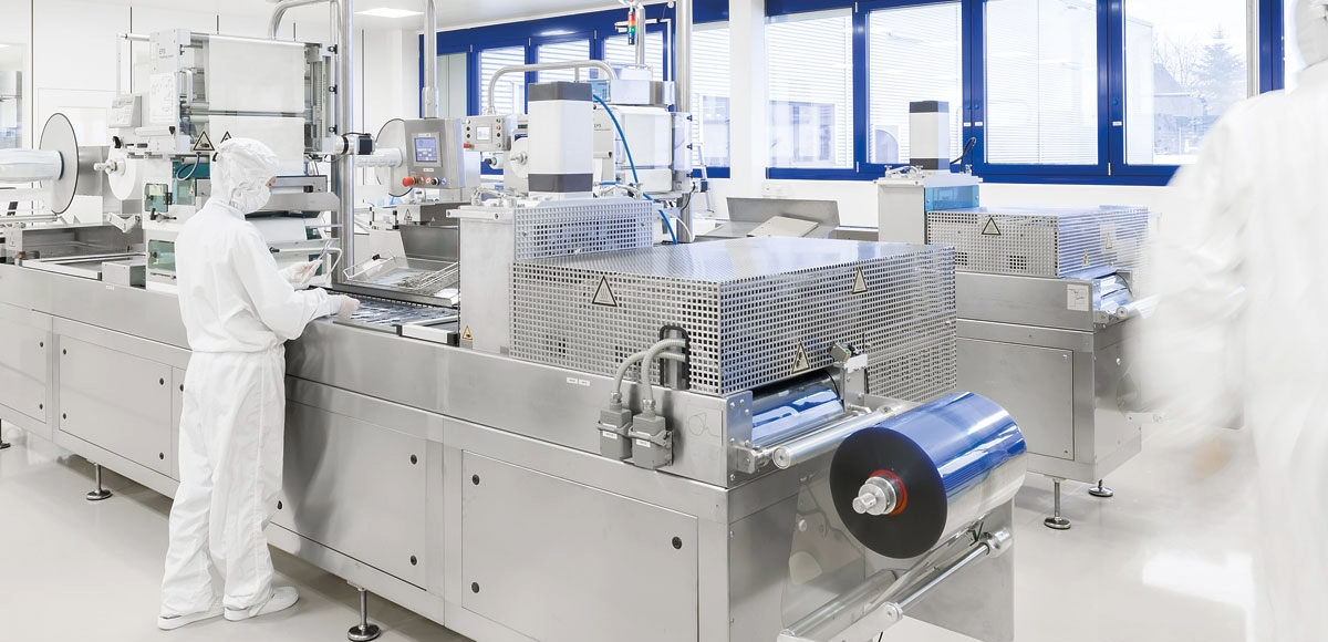 Production machine manufacturing sterile blister packaging with cleanroom personnel in the background.