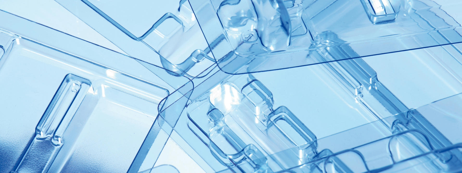 Close-up of transparent plastic packaging with multiple compartments and intricate shapes, featuring a blue tint from lighting or background.